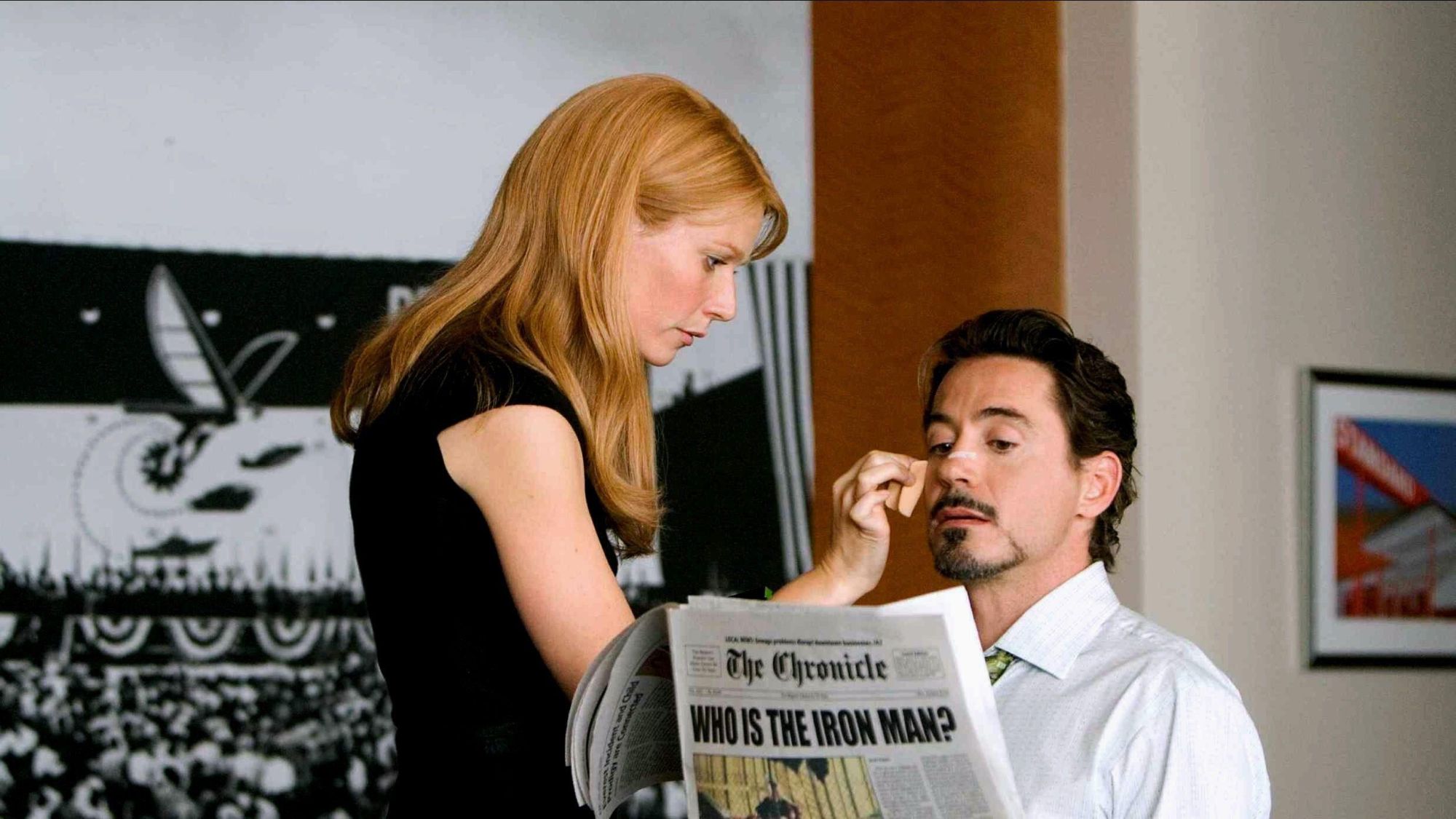 Gwyneth Paltrow applying makeup to Robert Downey Jr as he reads newspaper in Iron Man