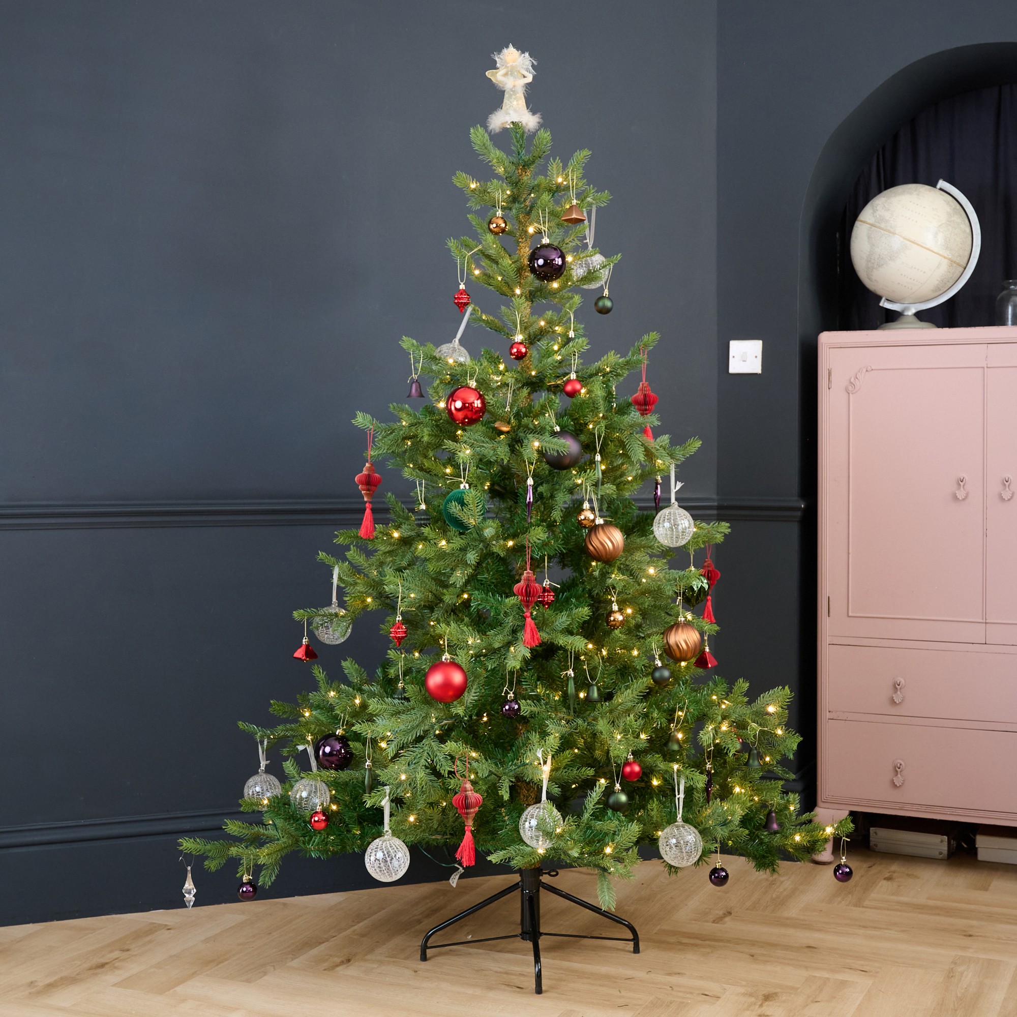 Cox & Cox's 6ft Bergen Spruce Pre-Lit Christmas Tree decorated with Christmas baubles in a black-painted living room