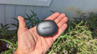 The EarFun Air S's charging case being held aloft a grassy backdrop
