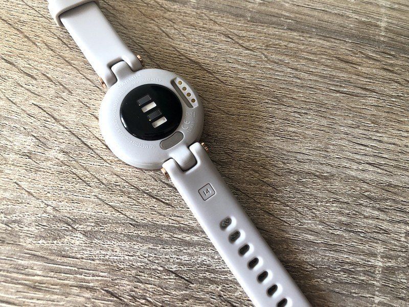 Garmin Lily smartwatch band laid out on a wooden table showcasing its backside and sensors.
