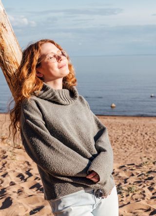 Young woman enjoying sunlight leaning on tree at a beach