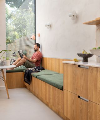 A man sat on a built-in banquette window seat reading a book