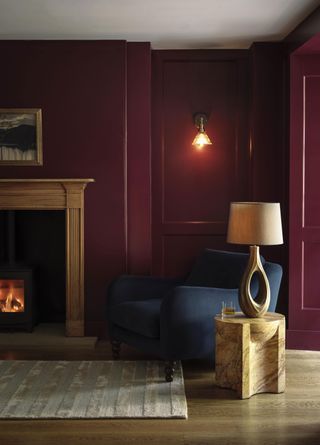 dark red living room with blue arm chair and open fire and wall lights