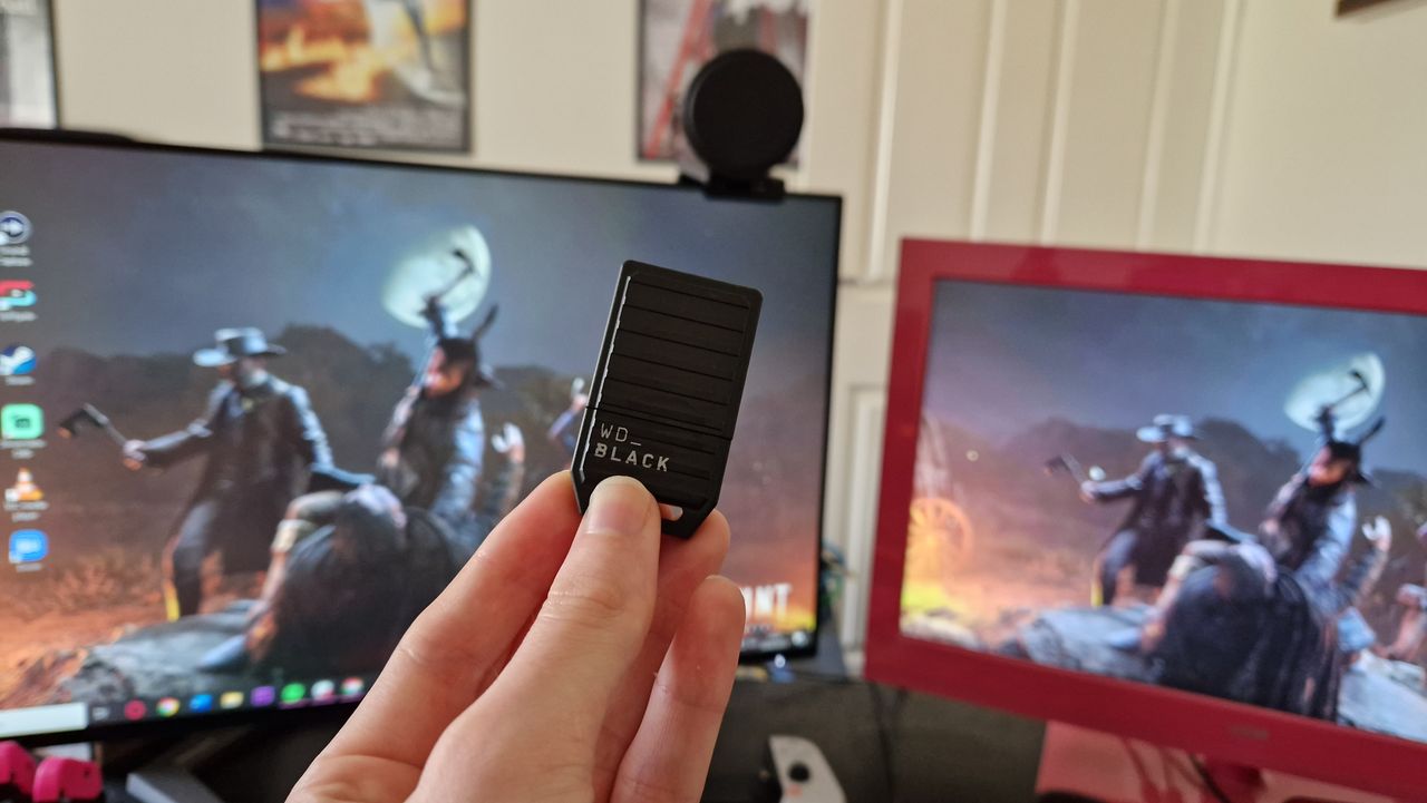 WD Black C5 held in front of two gaming monitors with its shield cover on