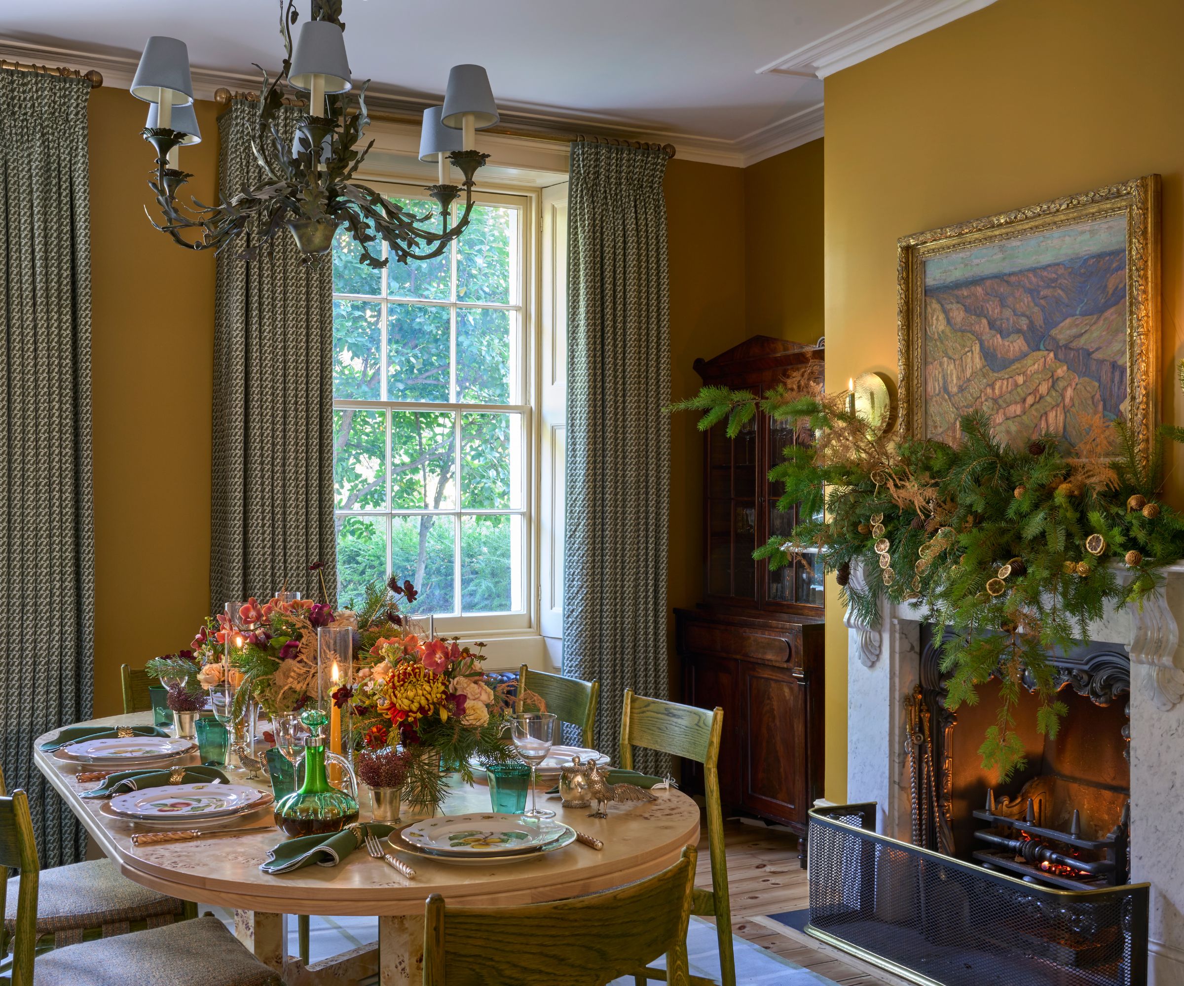 Yellow dining room decorated for Christmas with a garland above the fire and a round wooden table ready for guests