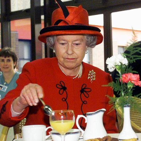 Queen Elizabeth wearing a red coat and hat stirring tea