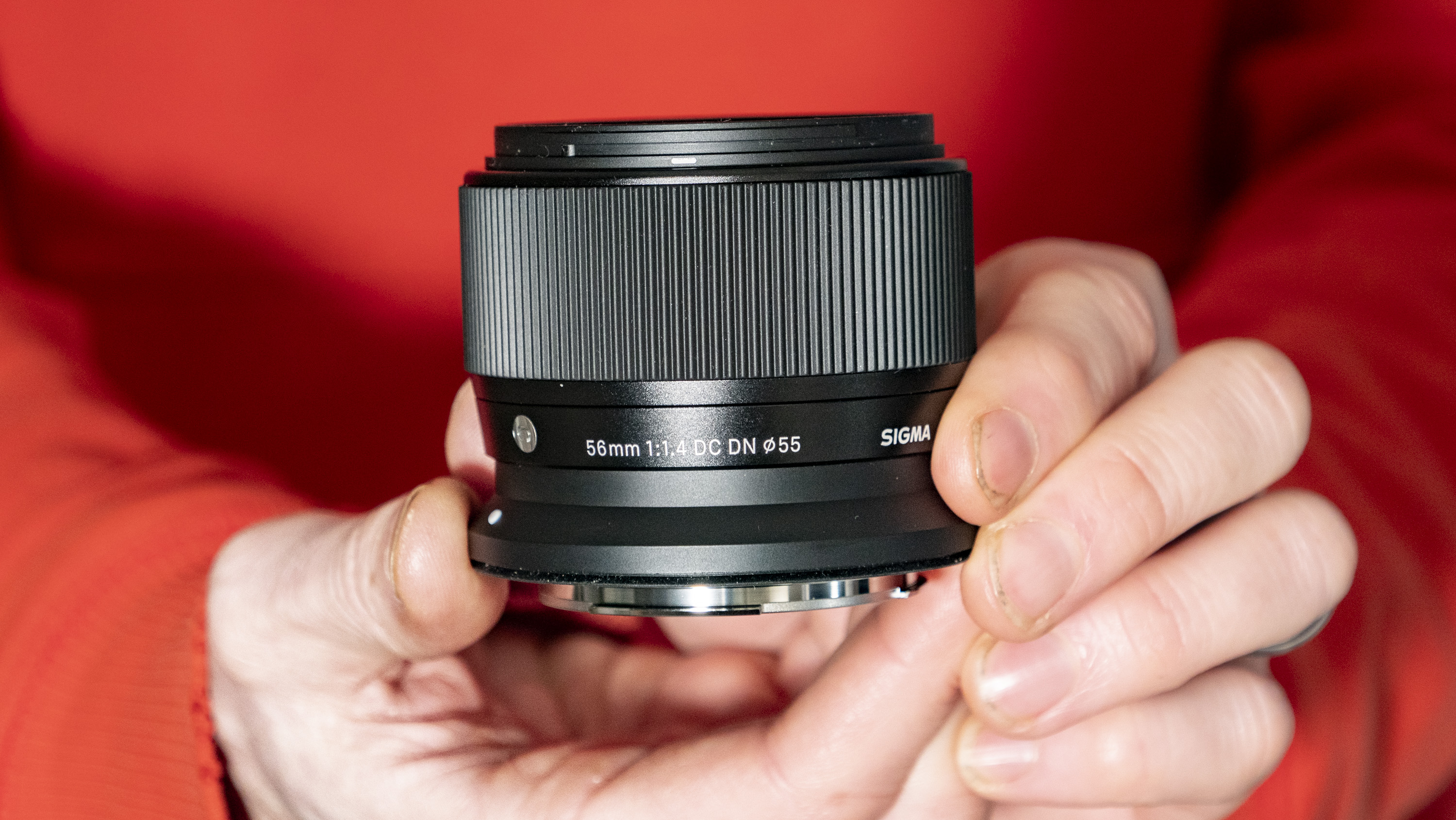 Sigma 56mm F1.4 DC DN Contemporary lens in the hand, orange T-shirt background