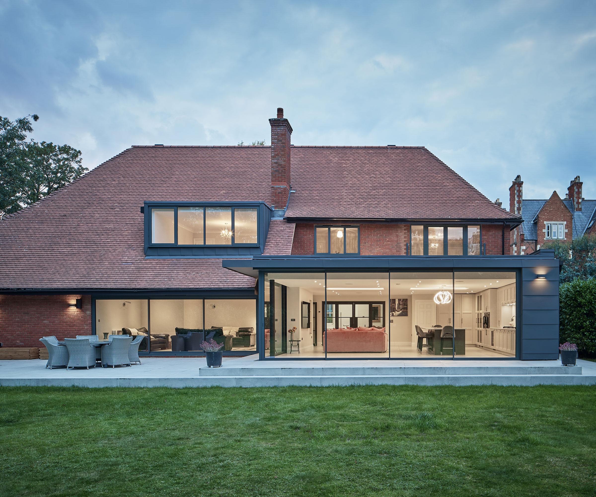 detached house with a large rear extension featuring sets of sliding glass doors leading out to a paved patio area