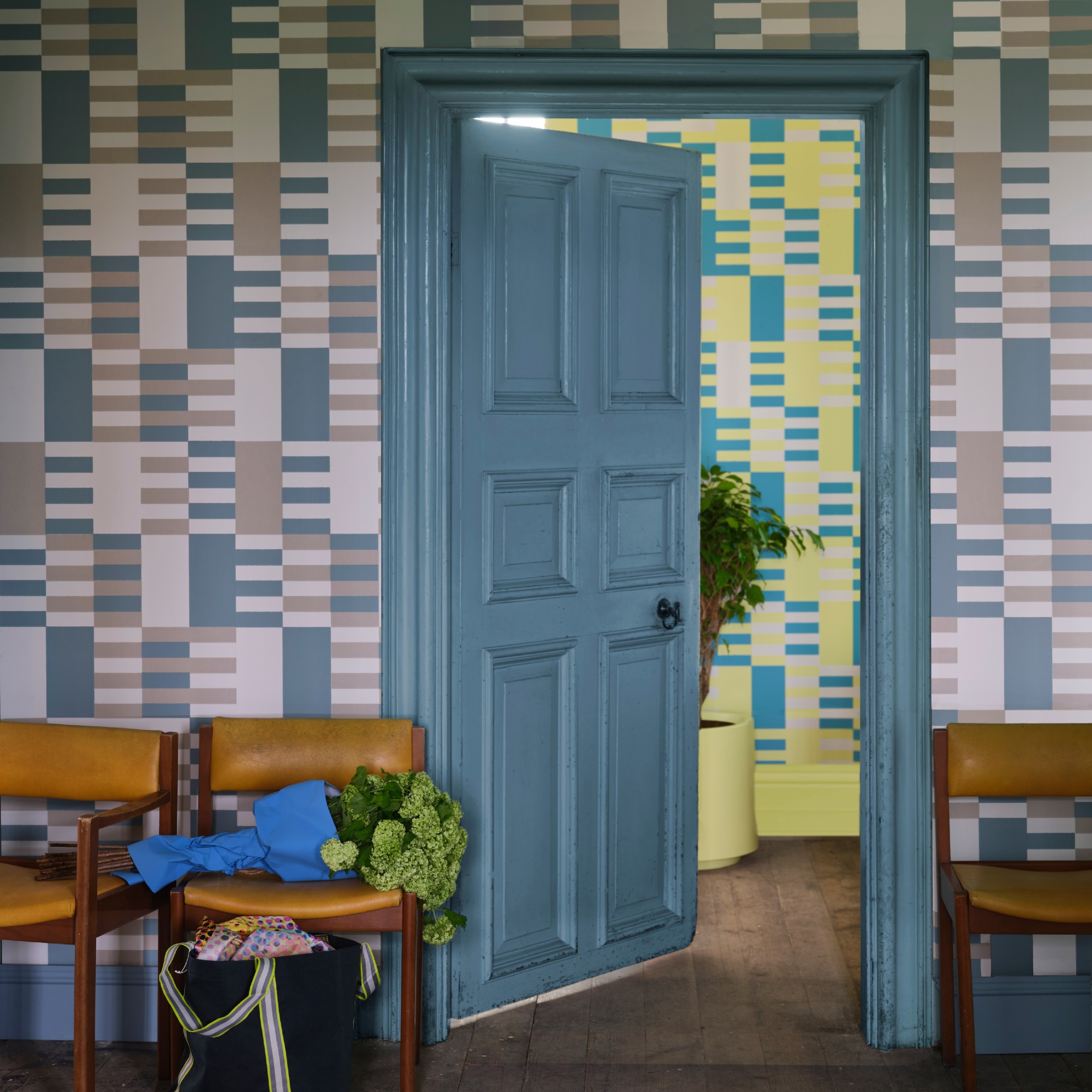 A hallway covered in a graphic wallpaper with a blue door painted in Farrow &amp;amp; Ball&#039;s Sardine