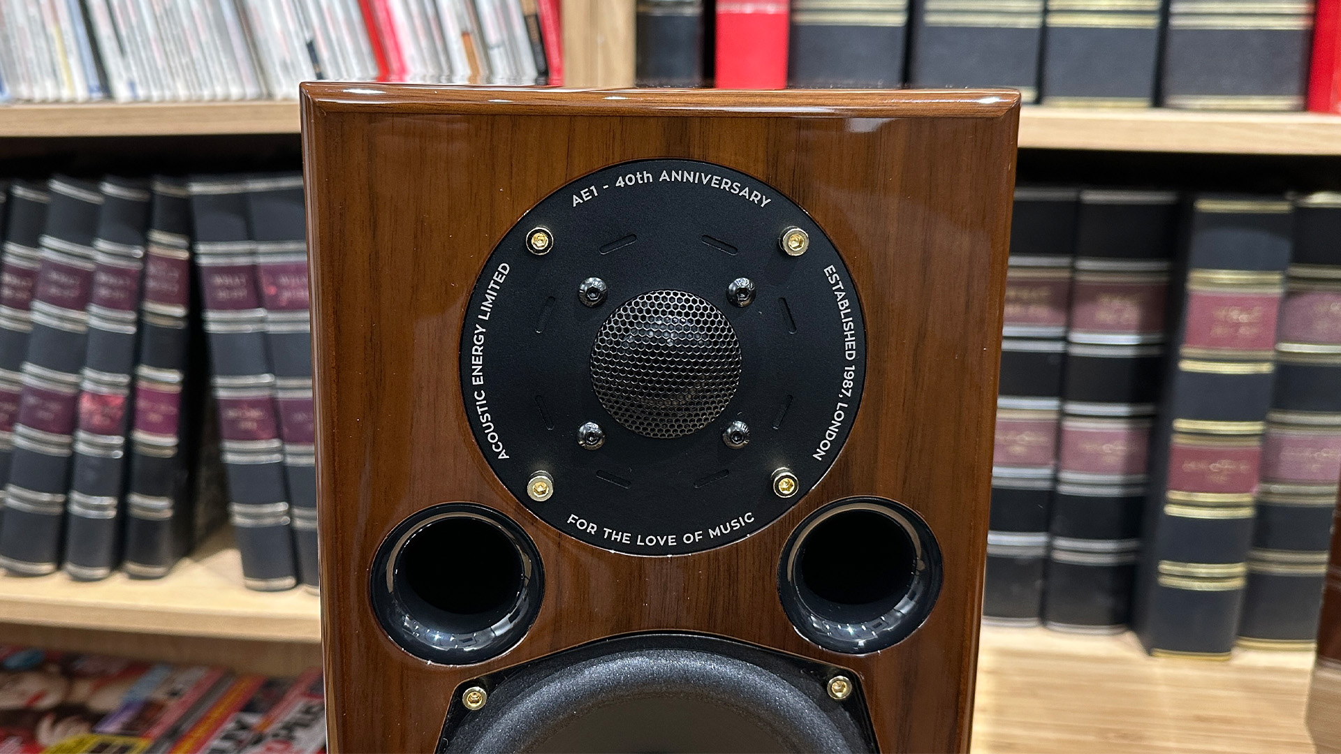 Acoustic Energy AE1 40th Anniversary standmount speaker on wooden hi-fi rack in front of bookcase