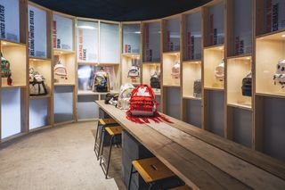 experiential brand design - interior of Eastpak shop, a bench with a rucksack on it and other rucksacks in cubby holes on the wall