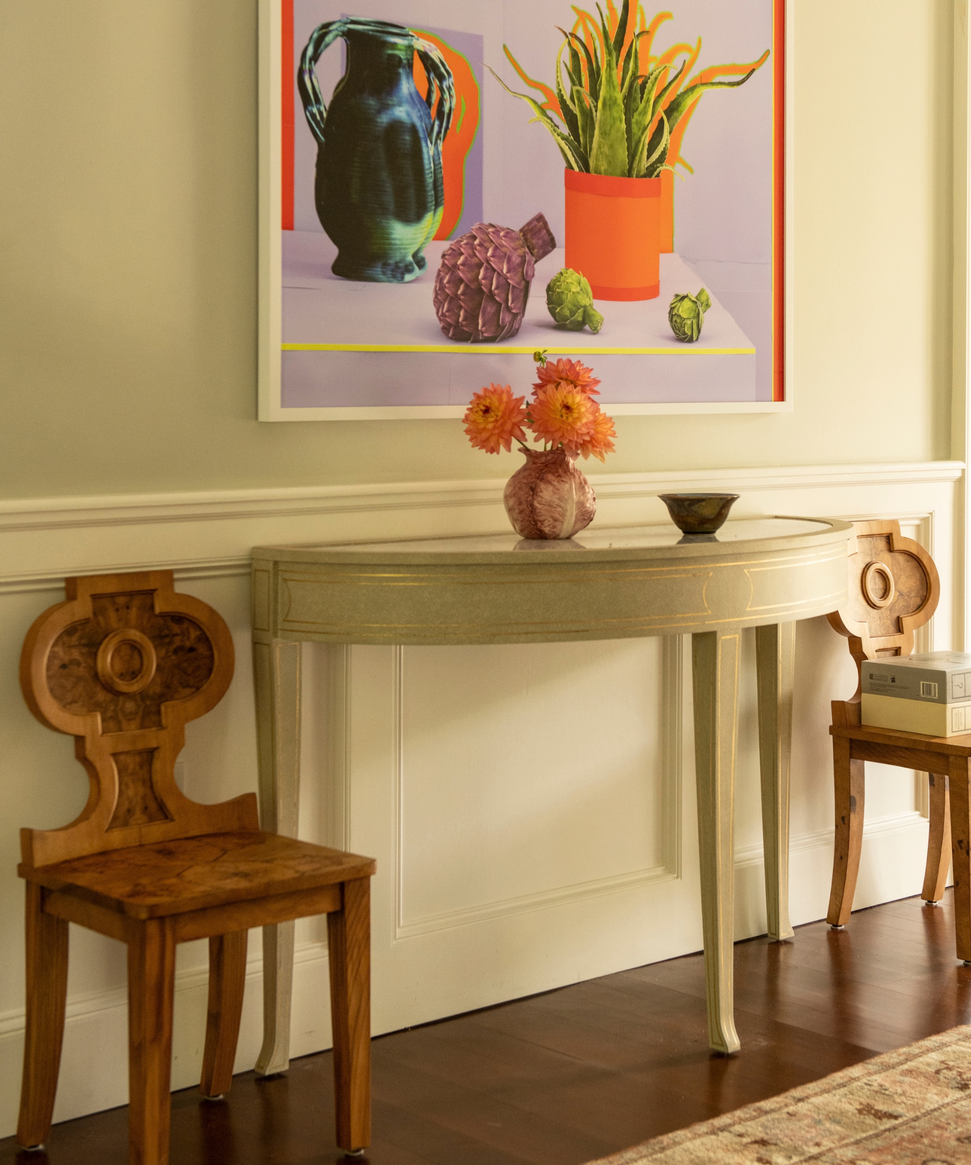 Light green console table flanked by two antique accent chairs with colorful modern wall art overhead