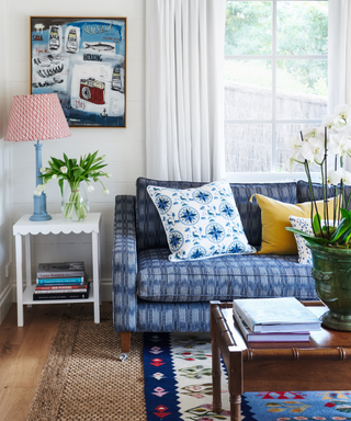 blue patterned sofa with cushions and side table with lampshade and art on wall and coffee table on rug with vase of flowers