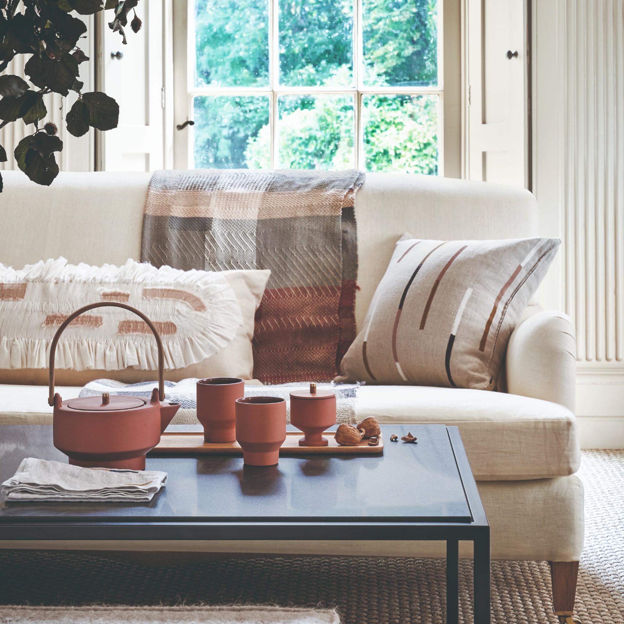 A bright living room with a cream sofa and a black coffee table with a tea set on top