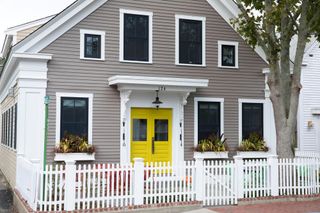 Traditional clapboard cottage with bright yellow front door and white paling fence at Provincetown, Cape Cod