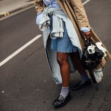 Street style featuring denim Bermuda shorts, a trench coat, loafers, and layered shirting.
