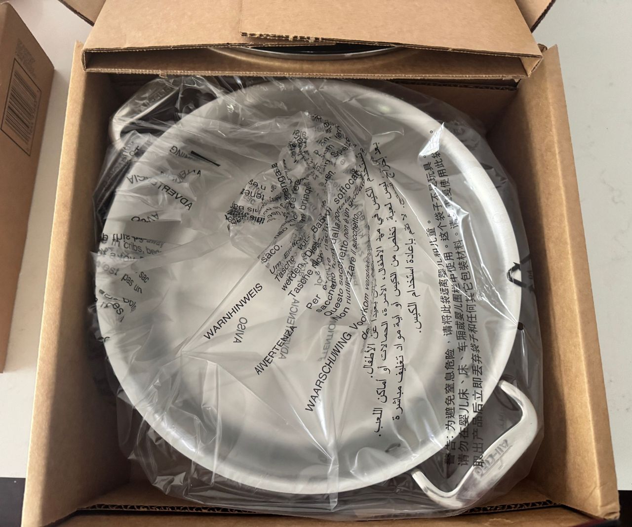 A stainless steel pot in a plastic bag, inside a cardboard box.