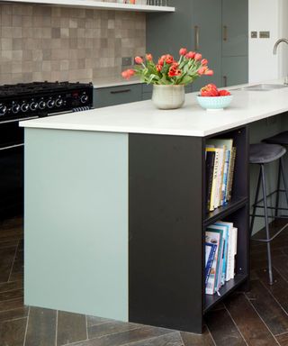 A kitchen island with a white countertop with flowers and fruit on it, a light blue base and a black shelf with books on it