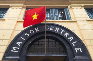 The arched entrance to the Hoa Lo Prison Museum in Hanoi with a red flag on top of it