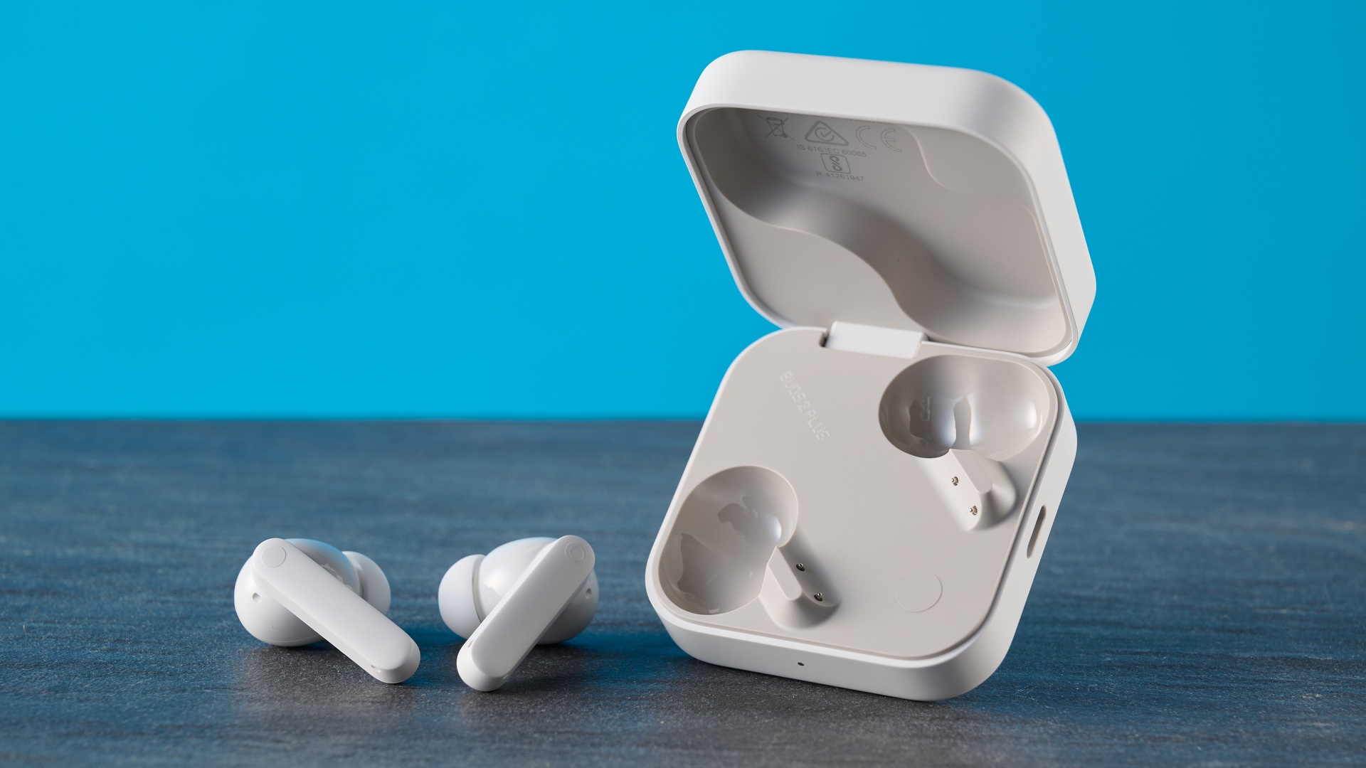 CMF Buds 2 Plus in light gray photographed in front of a blue background