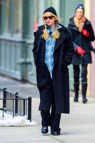 A photo of Jennifer Lawrence sporting blonde pigtail braids with a blue flannel skirt, a black coat, and a black beanie.