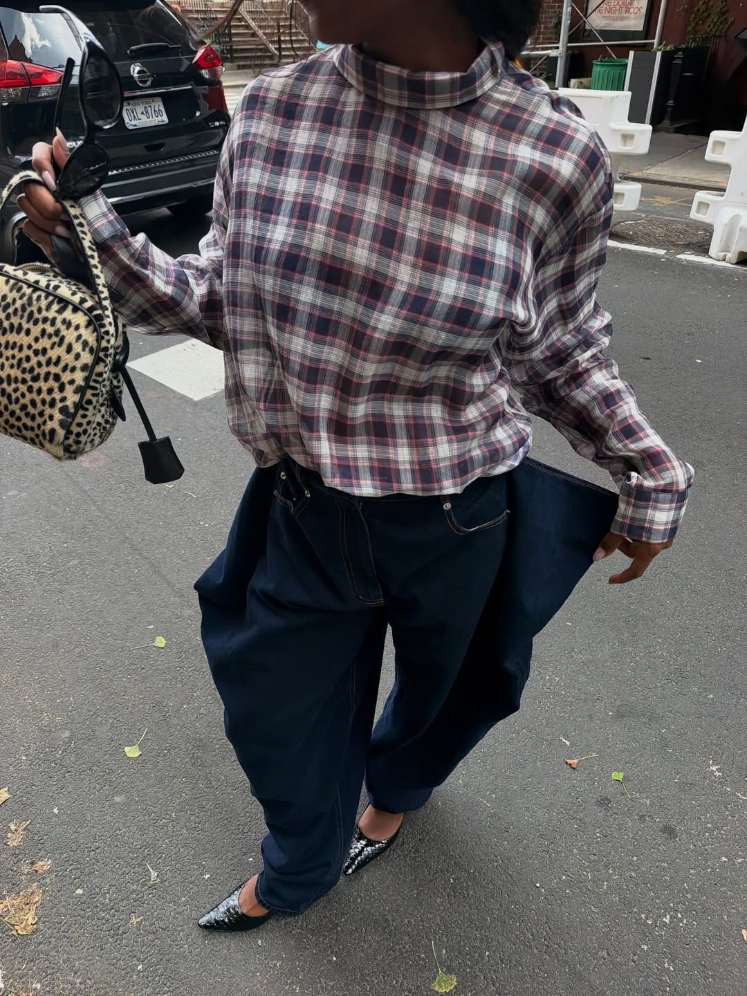 Devapollon shows how to wear a plaid shirt. She wears a backwards shirt with barrel-leg jeans, pointed-toe heels, and an animal-print bag.