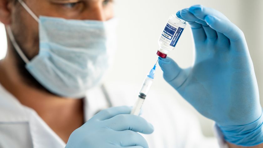 Close up of a medical professional holding a syringe drawing vaccine from a vial to prepare for injection.