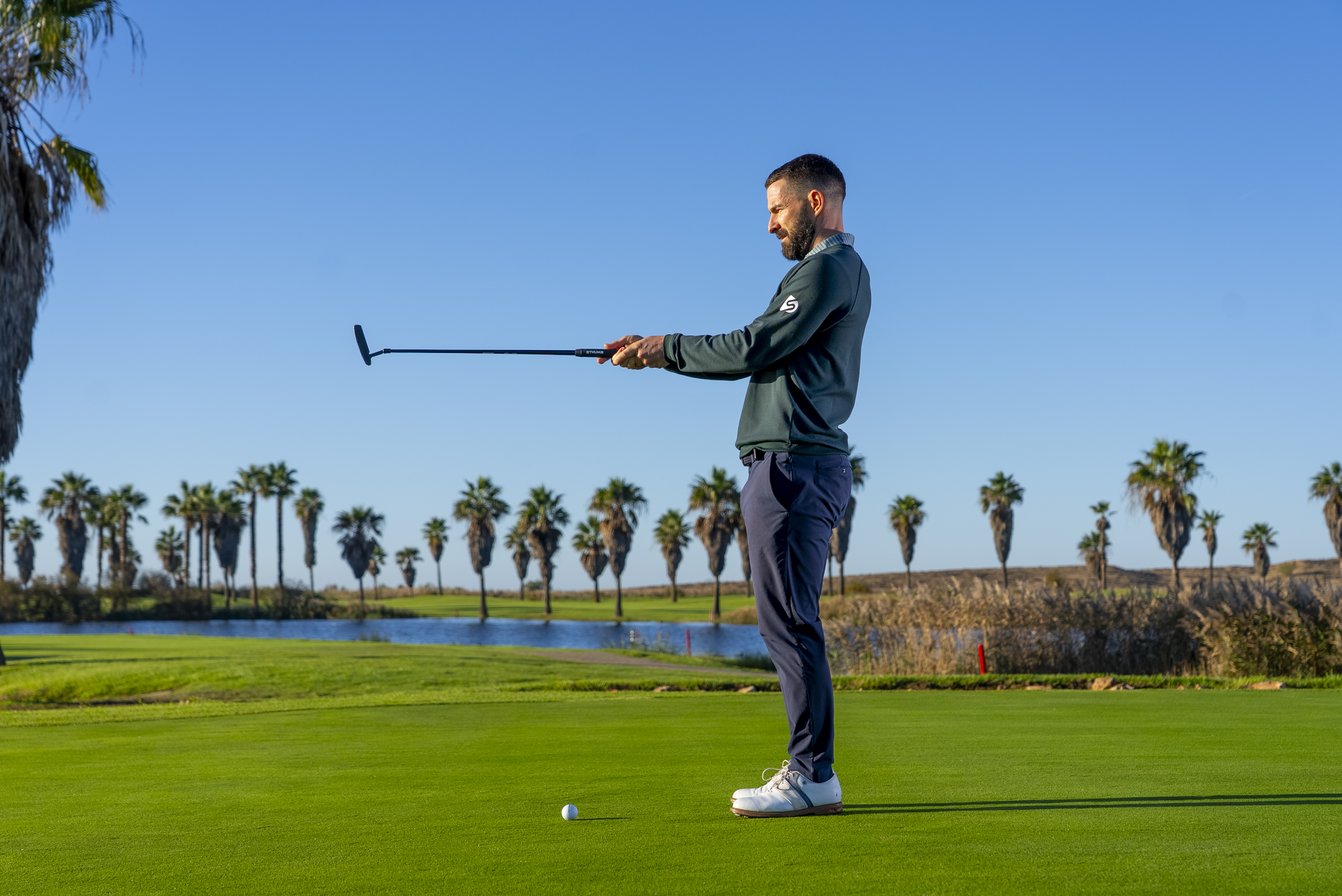 Putting Specialist Coach James Jankowksi reading a putt with his putter outstretched in front of him, similarly to how you would aim a gun