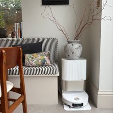 White robot vacuum cleaner with a stone vase sitting on top of the docking station in a kitchen