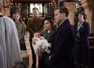 Rachel Shenton in a green coat as Helen holds baby Jimmy at his christening in the church while Nicholas Ralph in a dark overcoat as James, Callum Woodhouse in an army uniform as Tristan, Imogen Clawson in a green striped jacket as Jenny and Gabriel Quigley as Hannah Herriot look on in All Creatures Great and Small