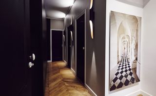 Interior view of the grey, black and white hallway at the Seine side apartment featuring wood flooring, wall lights and wall art