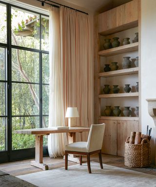 neutral bedroom with metal framed windows, wooden trestle table and shelves with ceramics