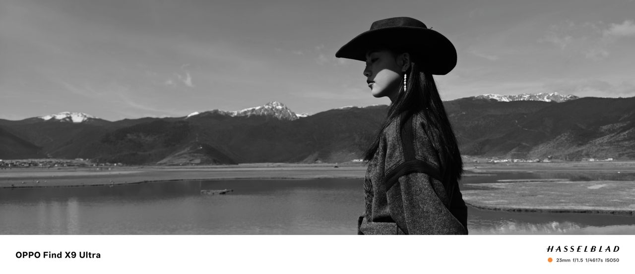 A woman in cowboy hat in front of a snowy mountain with lake, black and white