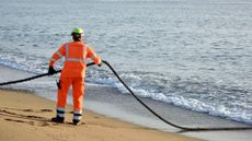 Worker on a beach holding an undersea internet cable