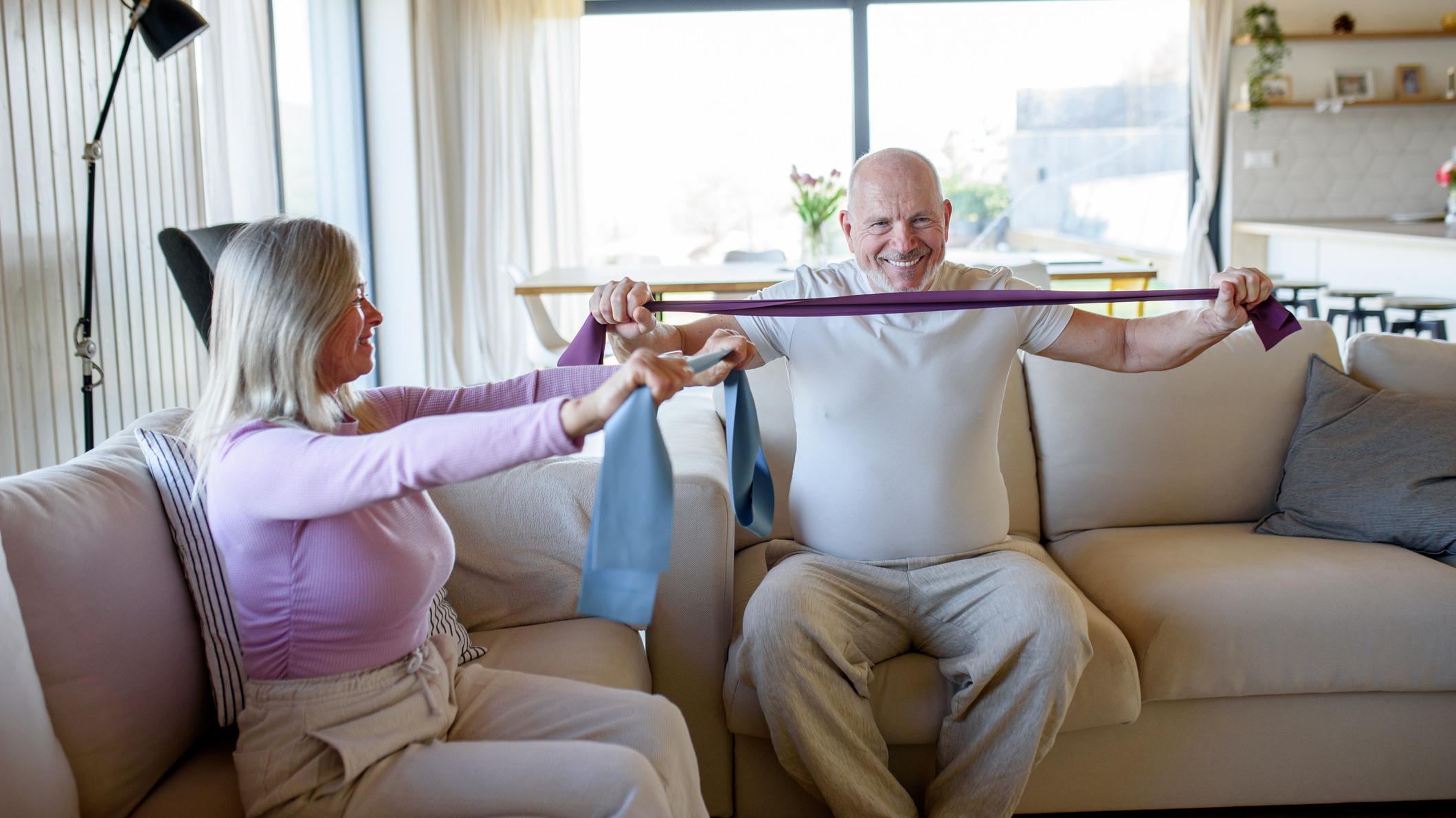 Man and woman sitting on a coach exercising with resistance bands