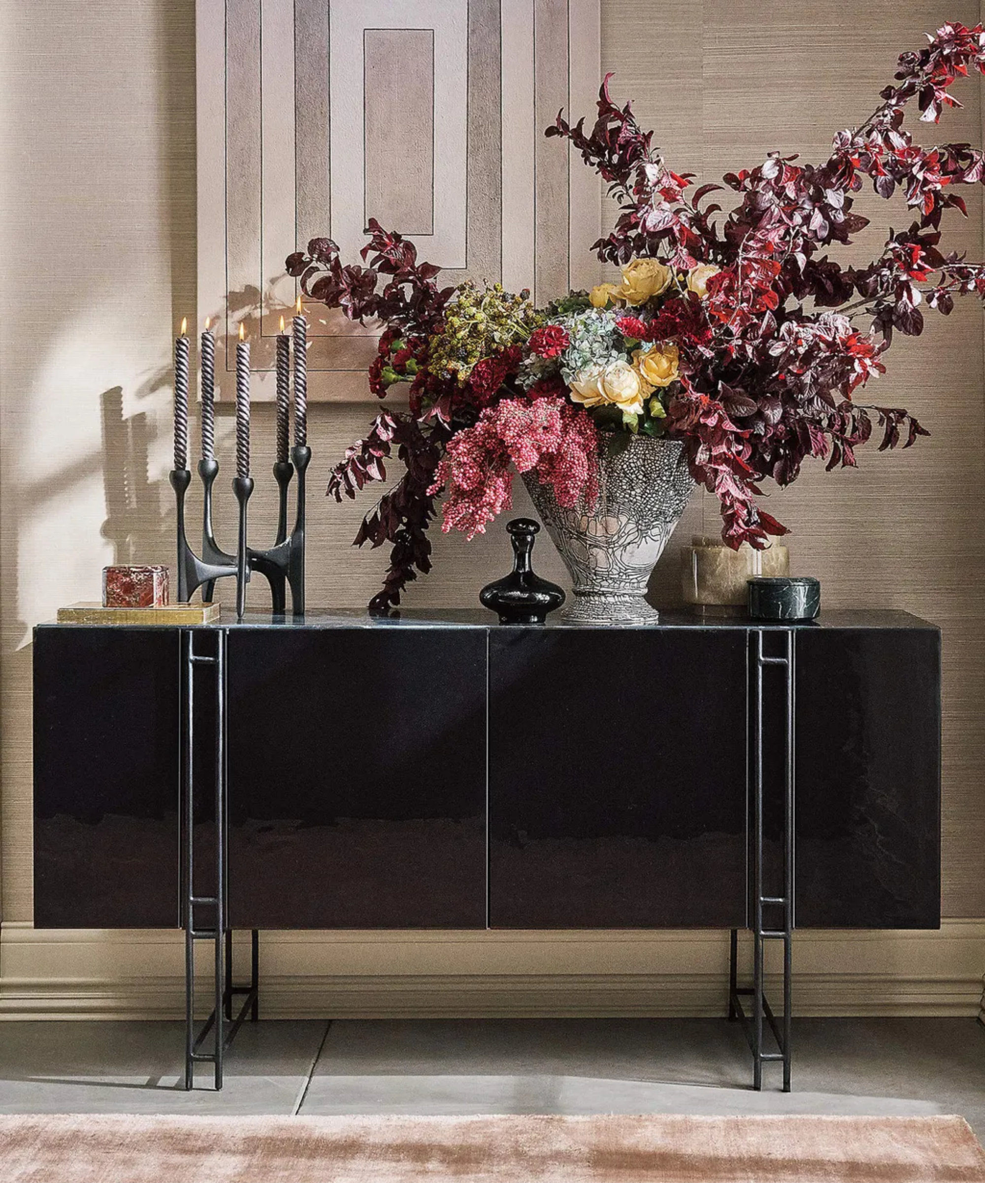 a credenza with a dark floral arrangement and candles