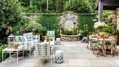 large flagstone patio with two seating areas and a water feature in a stone wall