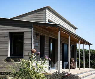 external shot of wooden clad home with overhang over patio area featuring black framed windows and patio doors