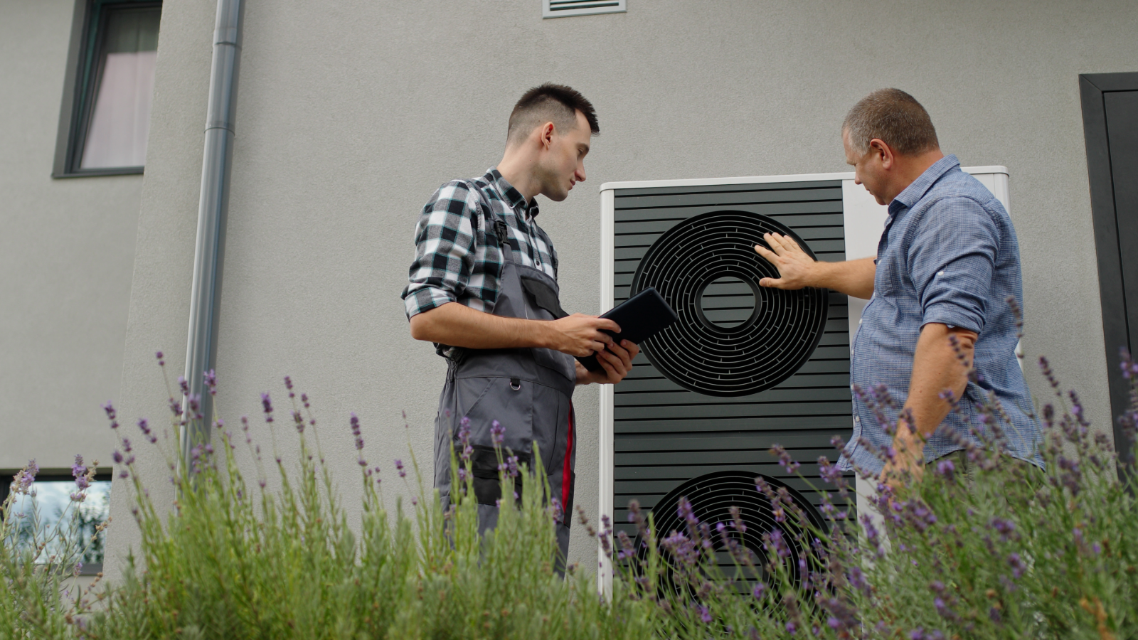 Two people standing next to a heat pump behind lavender