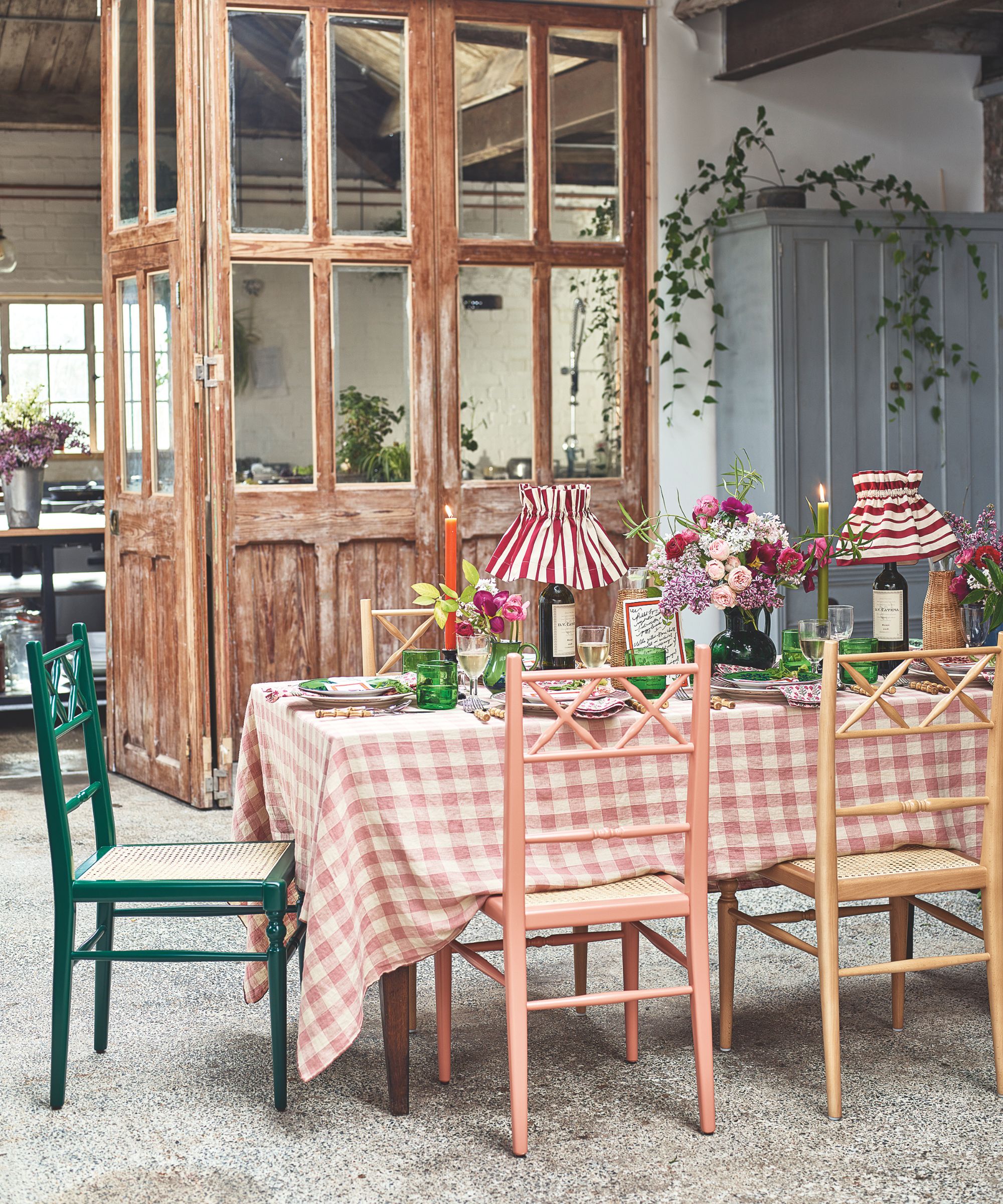 Garden room table setup with gingham table cloth, green glassware, wine bottle lamps and a rustic doorway in the background