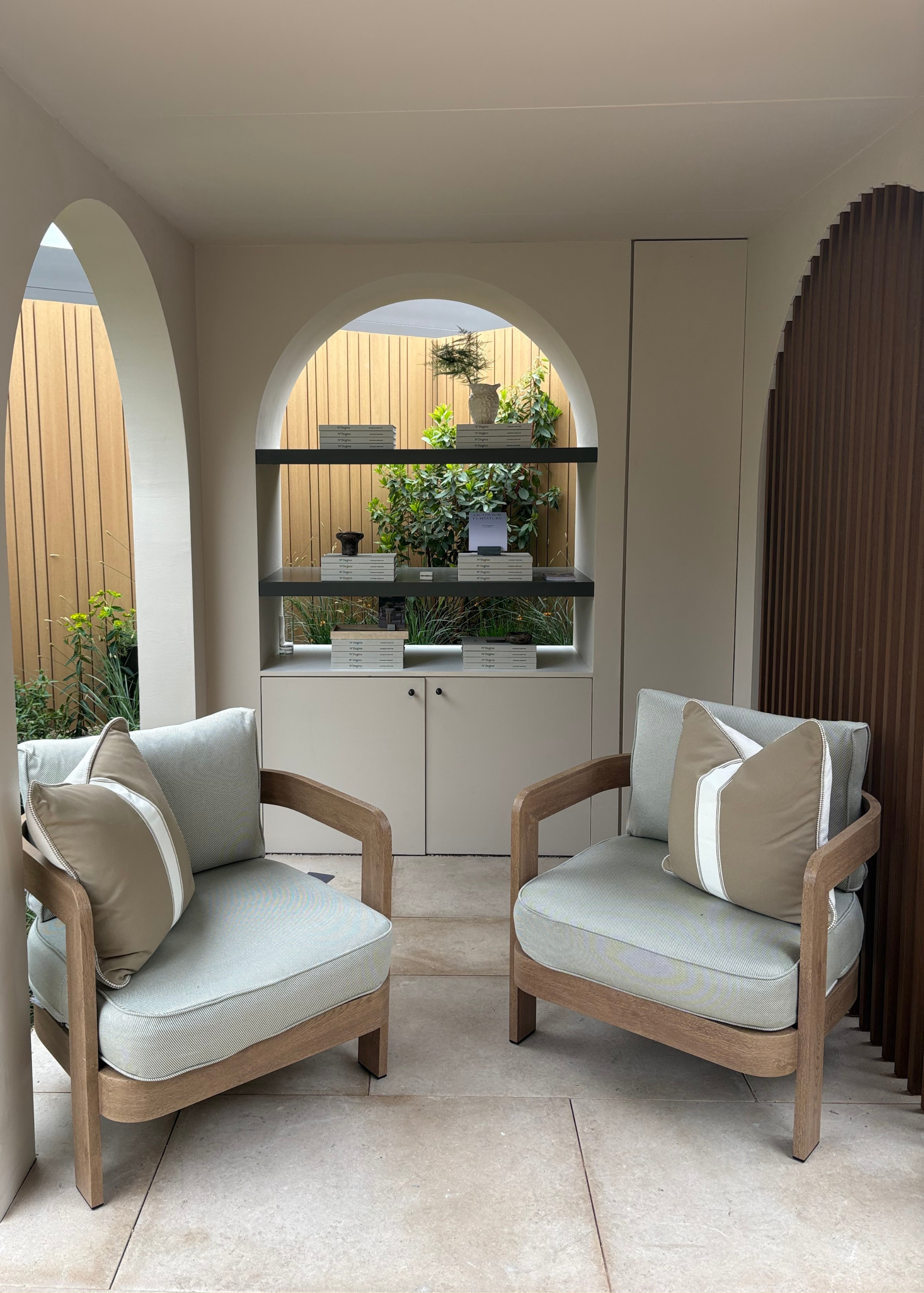 An outdoor space at the Chelsea Flower Show featuring Mediterranean garden design with a pair of outdoor sofa chairs