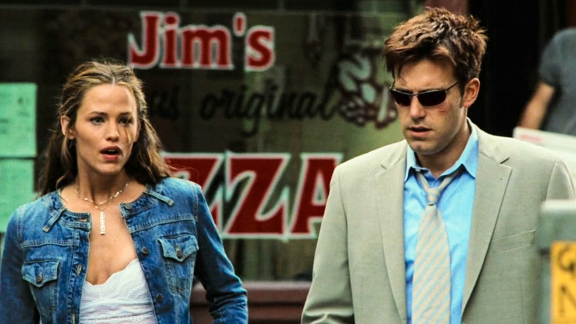 Elektra (Garner) dressed in denim jacket and white top walks with Matt Murdock (Affleck) in a tan suit with blue shirt, in Daredevil (2003).