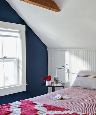 bedroom with sloped ceiling, white walls and navy blue accent wall, pink patterned bedding, wood ceiling beam and window