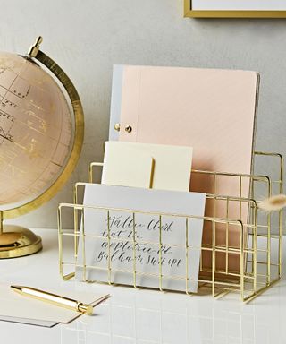 A gold metal letter rack with envelopes and paper decor, with pink rotating globe ornament