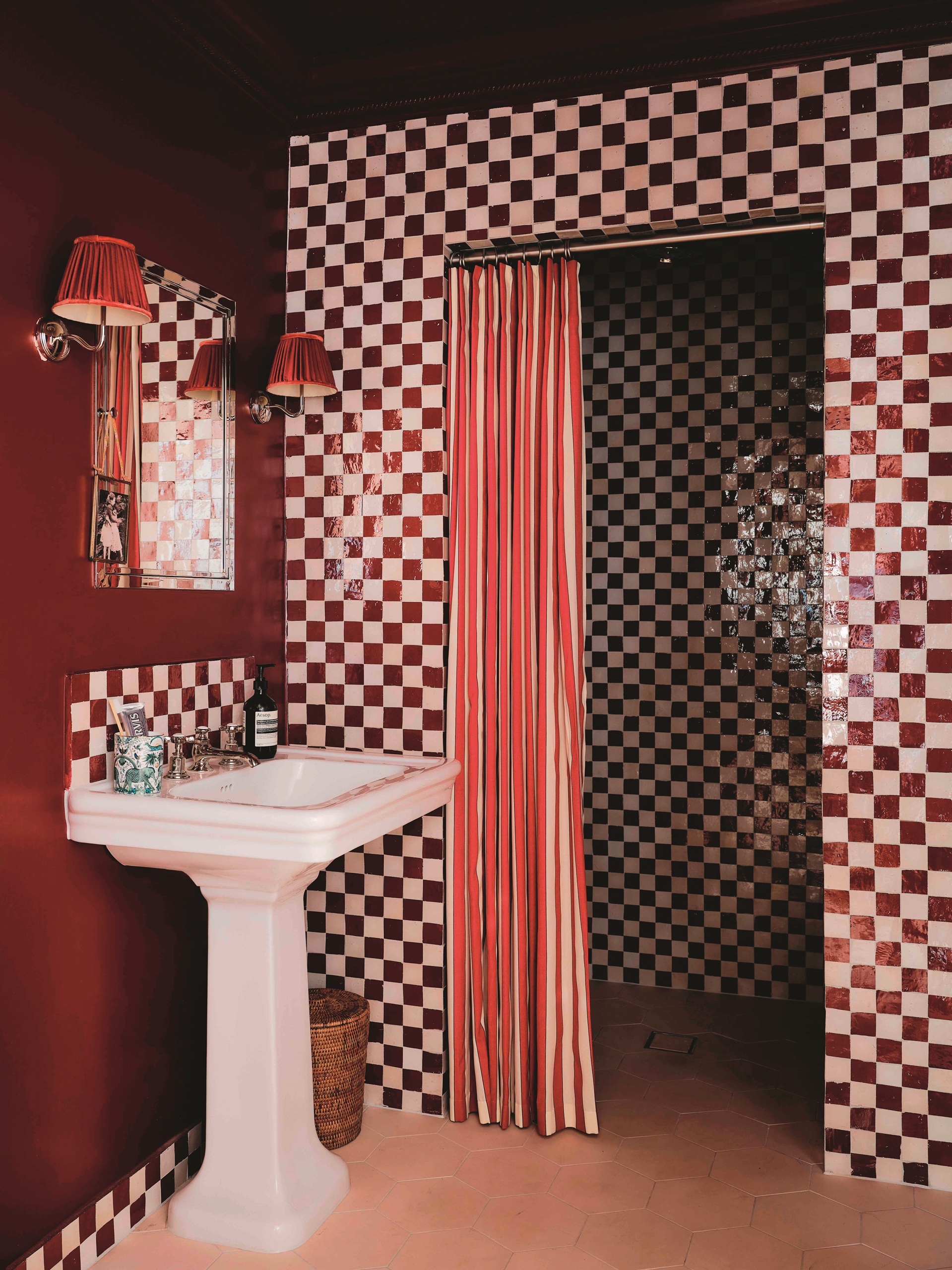 modern bathroom with checked tiles, striped shower curtain, pedestal basin with mirror on wall and two wall sconces and burgundy walls