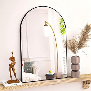 black rimmed arch mirror sitting on a fireplace with other accessories