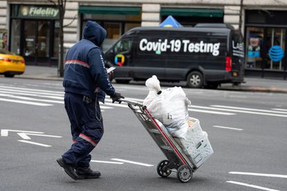 A USPS mail worker wheels a mail cart past a "COVID-19 Testing" location 