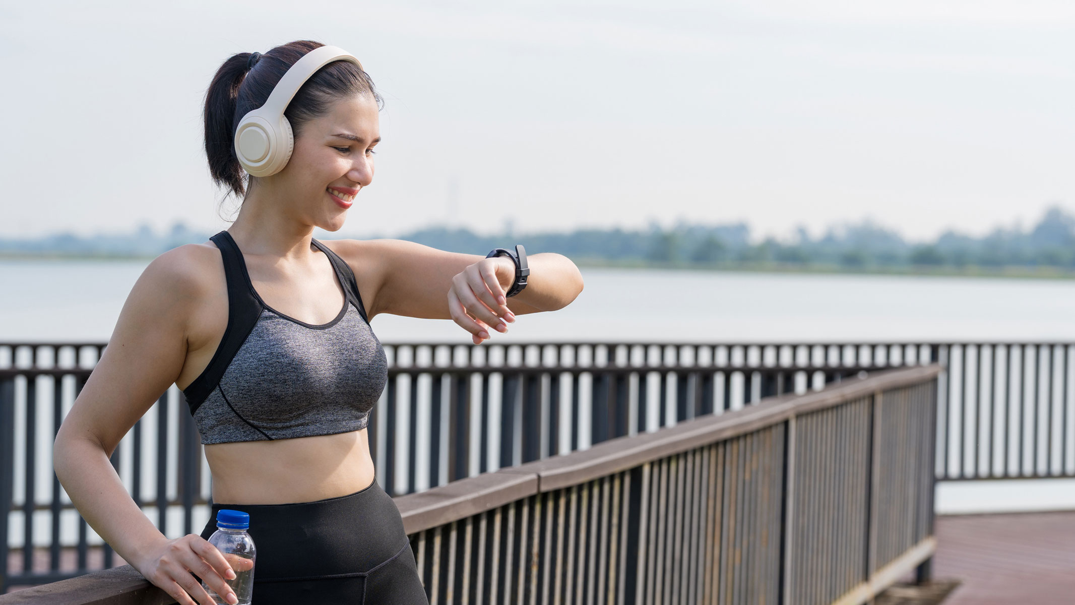 A picture of a woman smiling while checking her smartwatch on a run outside