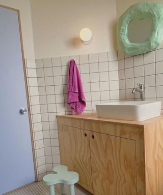 Bathroom with white tiled walls, green pastel stool and mirror, and purple door