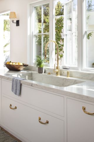 A gold faucet with a stone sink and a bright window